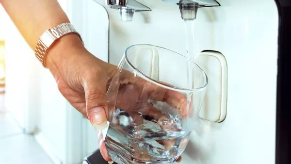 pessoa pegand água no purificador com copo de vidro