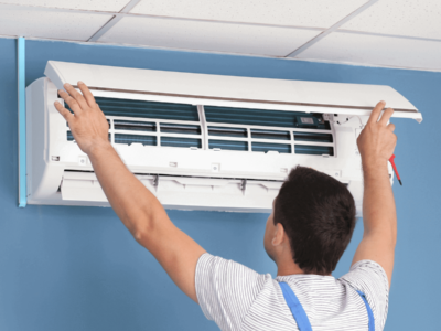 Homem técnico em refrigeração dando manutenção em um ar condicionado preso em uma parede azul